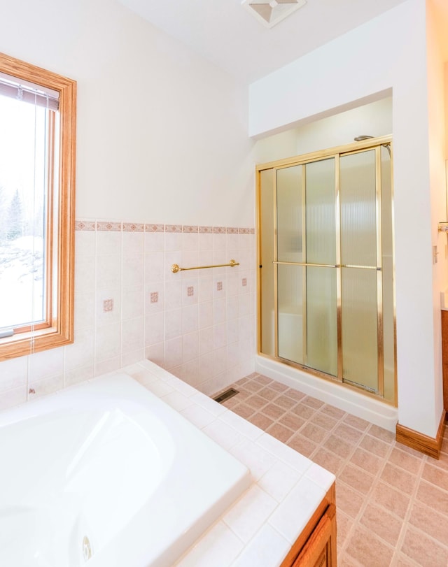 bathroom with a stall shower, a garden tub, visible vents, and tile walls