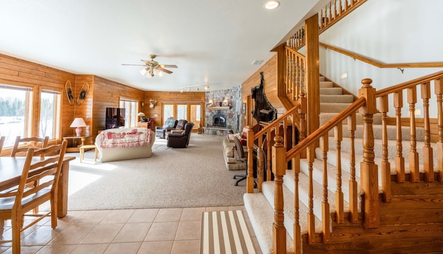 carpeted living room with stairs, a stone fireplace, tile patterned flooring, and a healthy amount of sunlight