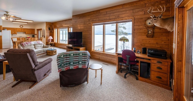 living area with light carpet, ceiling fan, and wooden walls