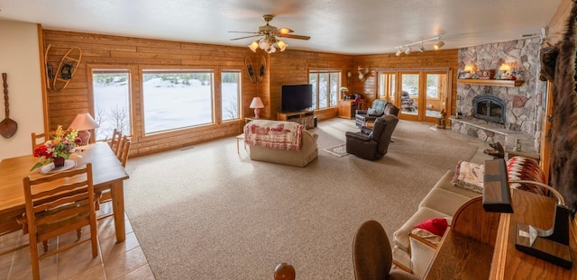 carpeted living area with a stone fireplace, a ceiling fan, rail lighting, and wooden walls