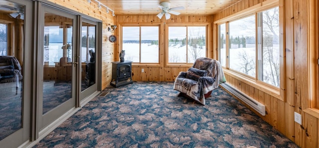 sunroom / solarium featuring a baseboard heating unit, a wood stove, wooden ceiling, and a wealth of natural light