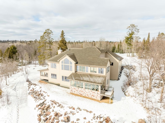 snow covered back of property featuring a chimney and a view of trees