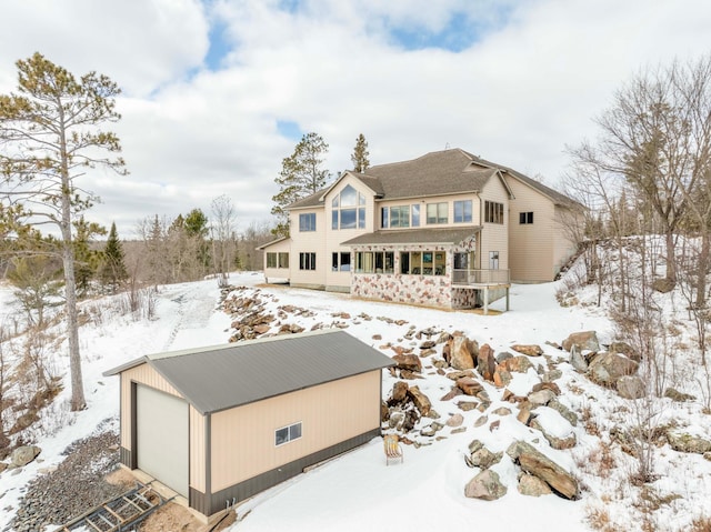 snow covered rear of property featuring a garage and an outdoor structure