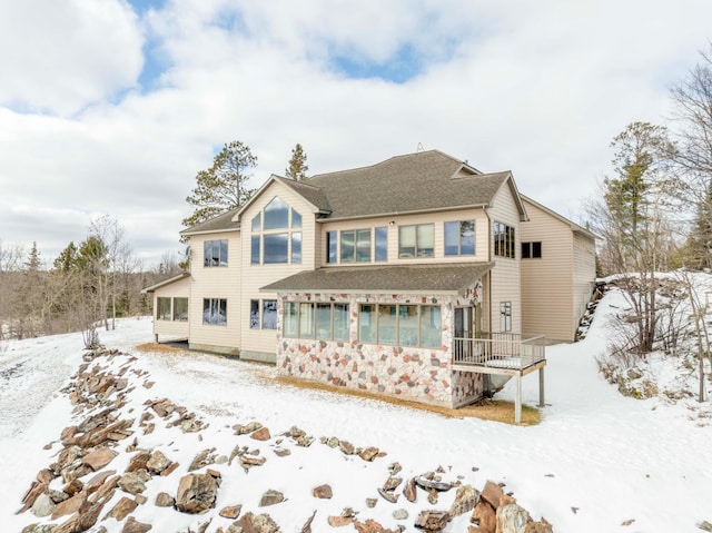 snow covered house with a sunroom and roof with shingles