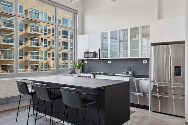 kitchen with white cabinets, a towering ceiling, finished concrete floors, stainless steel appliances, and a sink