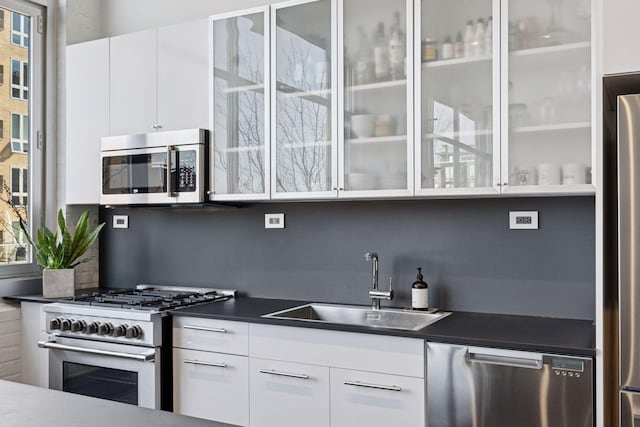 kitchen with dark countertops, modern cabinets, stainless steel appliances, white cabinetry, and a sink