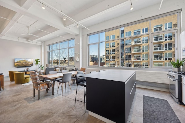 kitchen featuring rail lighting, concrete floors, beamed ceiling, and stainless steel stove