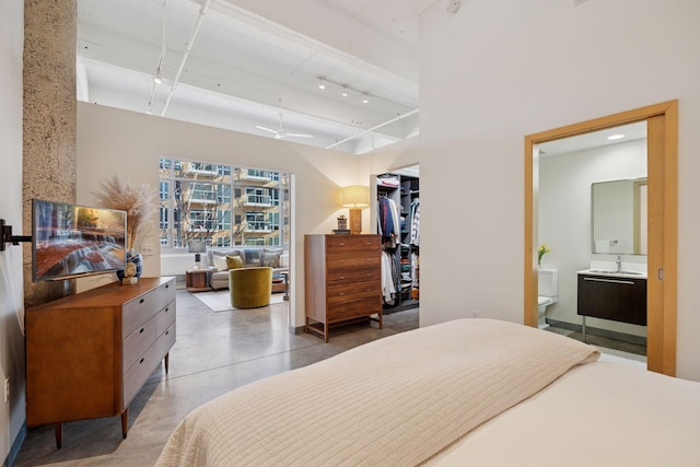 bedroom with a walk in closet, finished concrete floors, a sink, track lighting, and ensuite bath