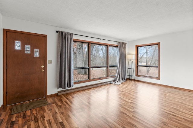 entryway featuring a baseboard heating unit, a textured ceiling, wood finished floors, and baseboards