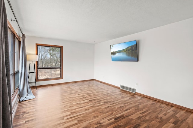 spare room featuring visible vents, a textured ceiling, baseboards, and wood finished floors