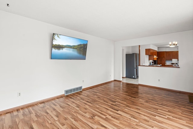 unfurnished living room featuring a chandelier, visible vents, light wood-style flooring, and baseboards