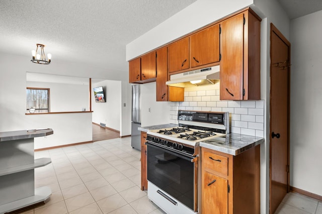 kitchen with brown cabinetry, backsplash, under cabinet range hood, and white gas range oven