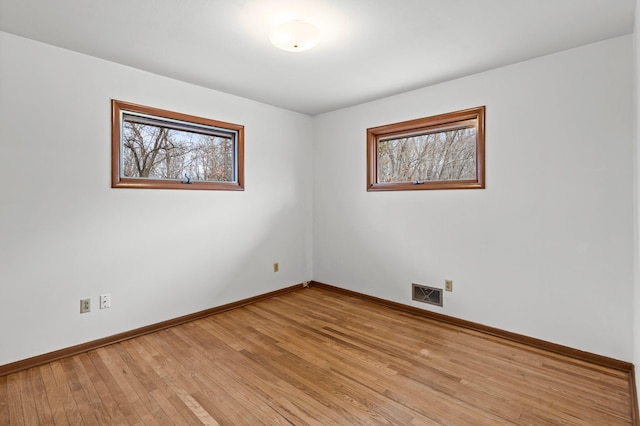 spare room featuring light wood finished floors, baseboards, visible vents, and a wealth of natural light