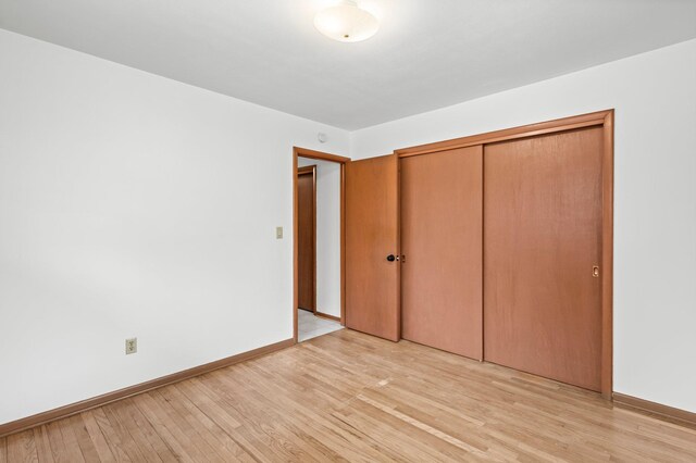 unfurnished bedroom with light wood-type flooring, baseboards, and a closet