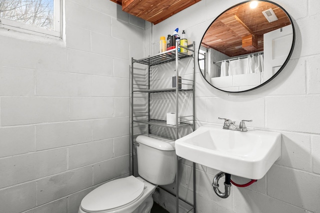 bathroom with toilet, a sink, and concrete block wall