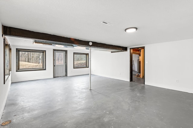 basement featuring visible vents, a textured ceiling, and baseboards