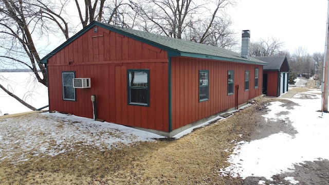 43404 Bills Beach Rd, Edna Twp, MN 56528 - view of snow covered exterior featuring a chimney, roof with shingles, and an AC wall unit