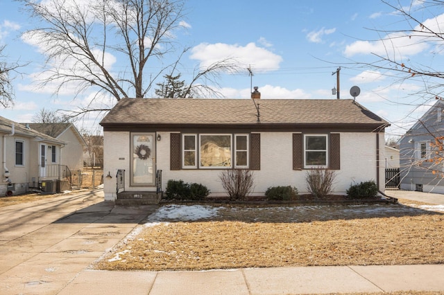 view of front facade featuring brick siding, a chimney, central air condition unit, a shingled roof, and entry steps