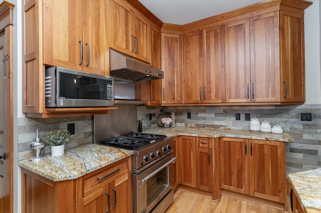 kitchen with light stone countertops, under cabinet range hood, stainless steel appliances, and brown cabinetry