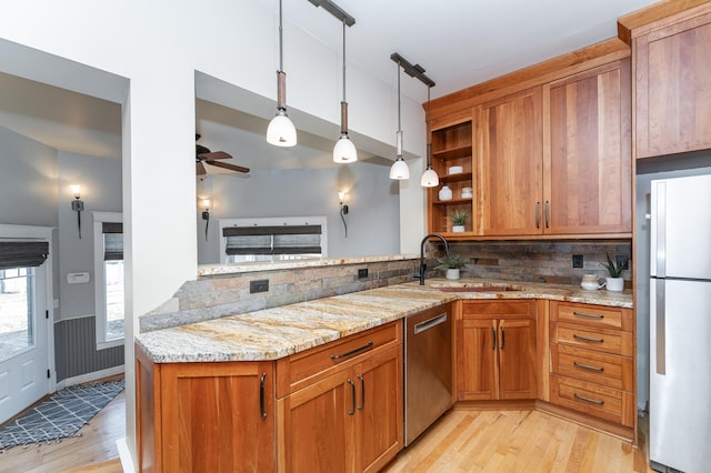 kitchen with brown cabinets, decorative light fixtures, freestanding refrigerator, light stone countertops, and a sink