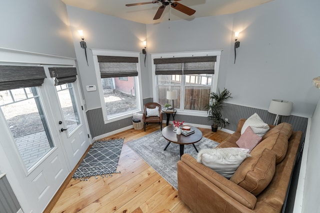 living room featuring light wood-style floors, a ceiling fan, and a wainscoted wall