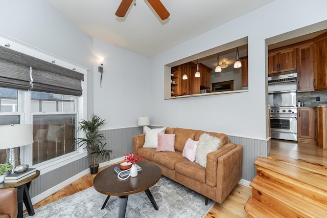 living area featuring a wainscoted wall, a ceiling fan, and light wood-style floors