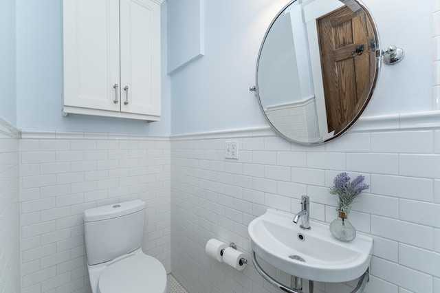 bathroom with a wainscoted wall, a sink, tile walls, and toilet