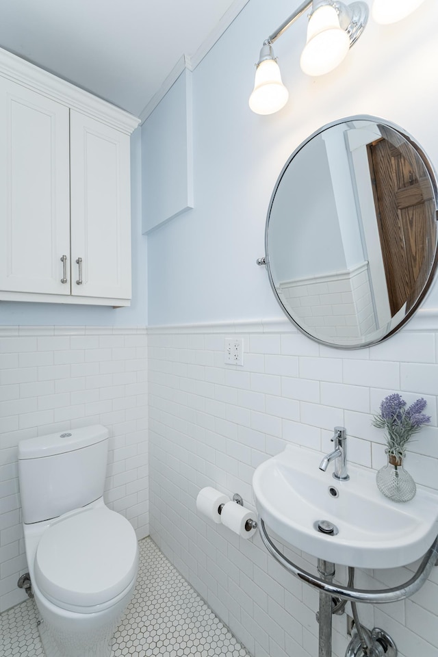 half bath featuring tile walls, wainscoting, toilet, tile patterned floors, and a sink