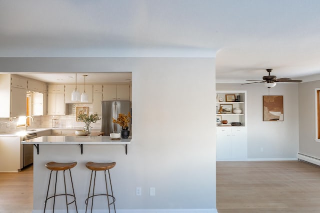 kitchen with light countertops, appliances with stainless steel finishes, backsplash, light wood finished floors, and a kitchen bar