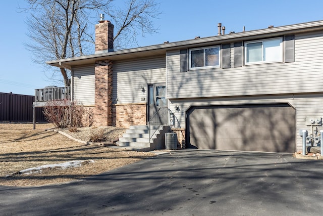 view of front of property featuring aphalt driveway, cooling unit, a garage, brick siding, and a chimney