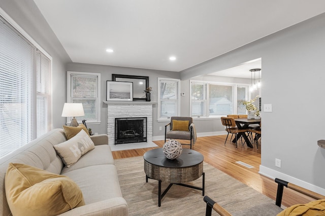 living room featuring light wood-style flooring, recessed lighting, a fireplace, visible vents, and baseboards