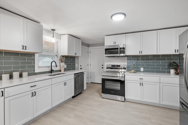 kitchen featuring hanging light fixtures, stainless steel appliances, light countertops, white cabinetry, and a sink