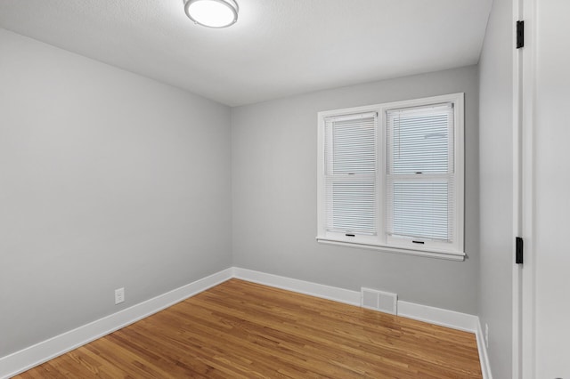 spare room with baseboards, visible vents, and wood finished floors