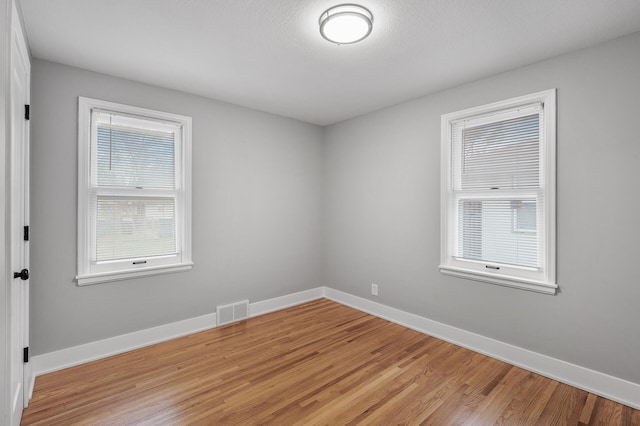 unfurnished room with light wood-style floors, visible vents, a textured ceiling, and baseboards