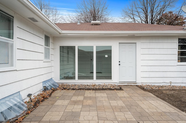 doorway to property with a shingled roof and a patio area