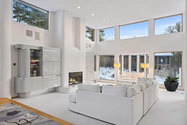 living area with a glass covered fireplace, light colored carpet, and a healthy amount of sunlight