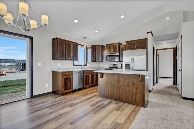 kitchen with pendant lighting, light wood-style flooring, appliances with stainless steel finishes, vaulted ceiling, and a kitchen island