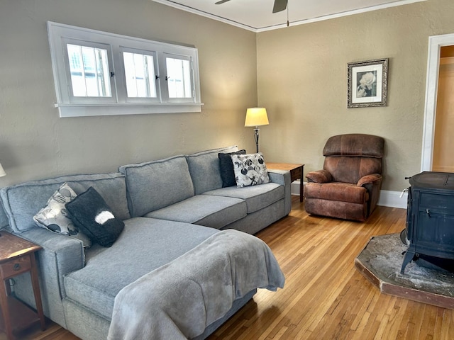 living area featuring a ceiling fan, baseboards, ornamental molding, light wood-type flooring, and a wood stove