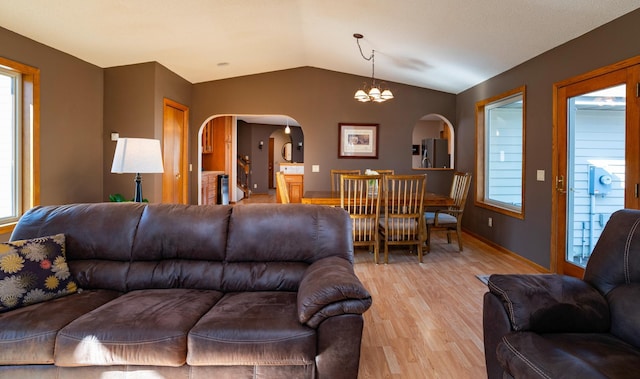 living room featuring arched walkways, baseboards, lofted ceiling, an inviting chandelier, and light wood-type flooring