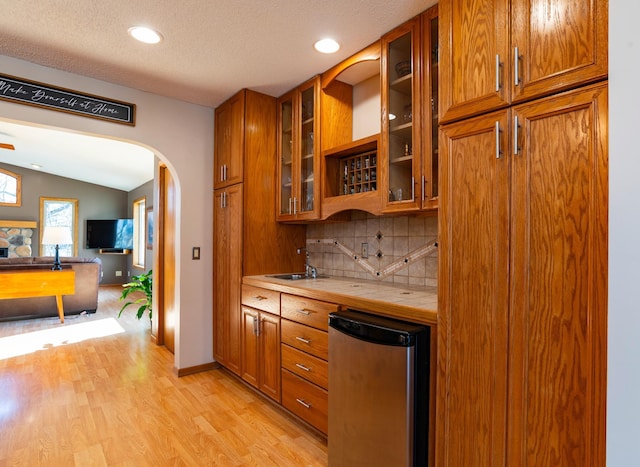 kitchen featuring tasteful backsplash, arched walkways, tile counters, brown cabinets, and refrigerator