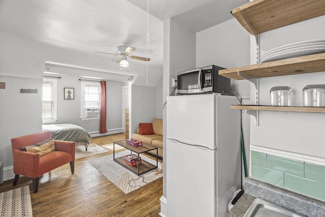 kitchen with wood finished floors, a baseboard radiator, freestanding refrigerator, ceiling fan, and stainless steel microwave