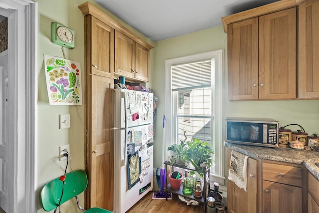 kitchen with brown cabinetry, stainless steel microwave, freestanding refrigerator, and light stone countertops