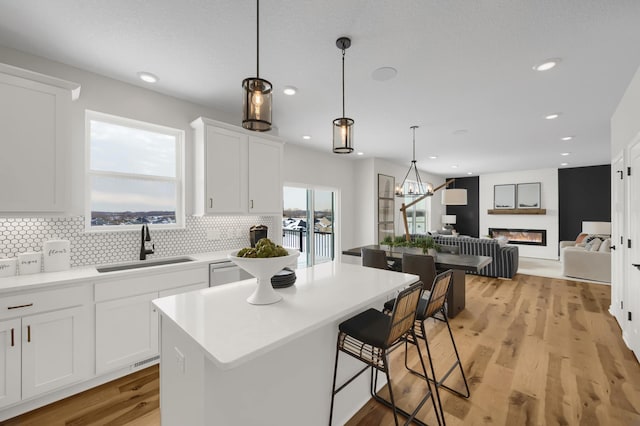 kitchen with tasteful backsplash, white cabinets, a glass covered fireplace, light wood-style floors, and a sink