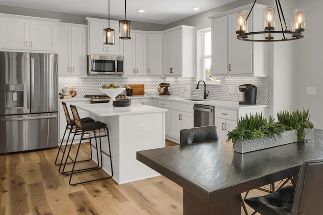 kitchen featuring decorative backsplash, appliances with stainless steel finishes, a center island, light countertops, and a sink