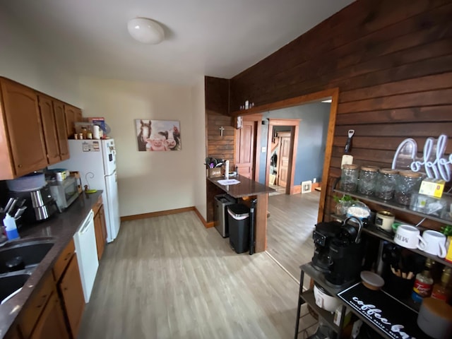 kitchen with dark countertops, wood walls, light wood-type flooring, white appliances, and a sink