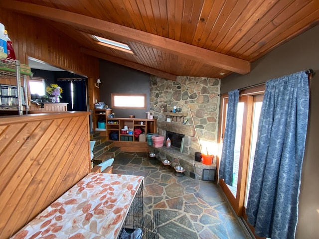 living area with plenty of natural light, stone floors, a stone fireplace, and wooden ceiling