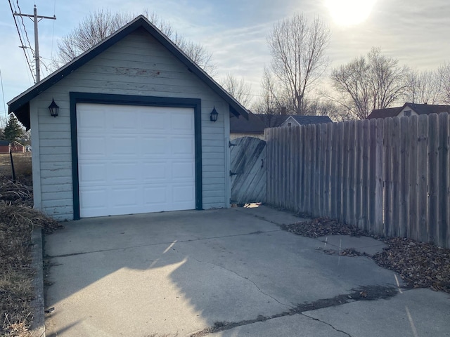 detached garage featuring concrete driveway and fence