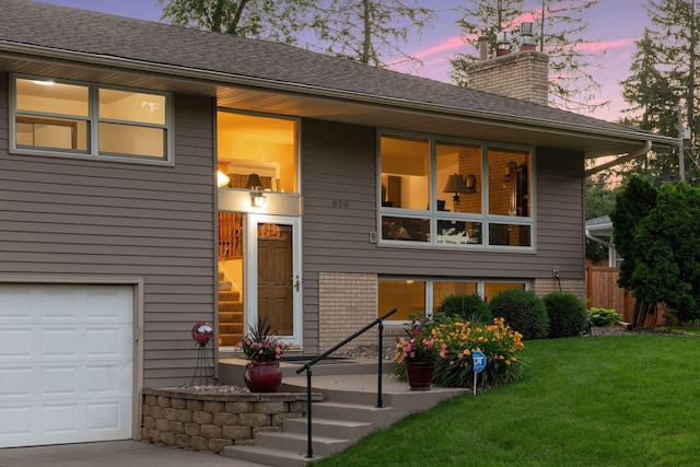 view of front of house featuring brick siding, a chimney, a lawn, fence, and a garage