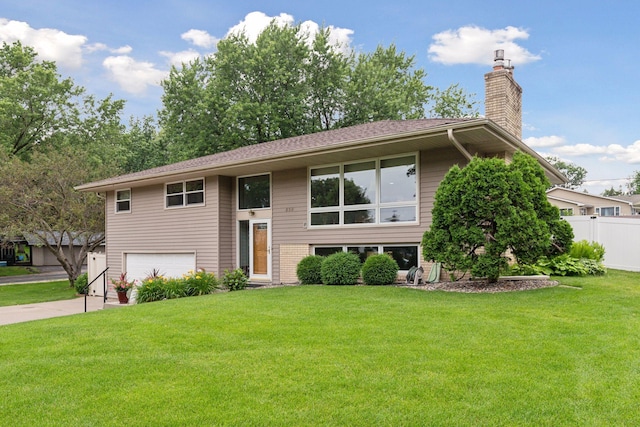 raised ranch featuring a front yard, fence, a chimney, and an attached garage