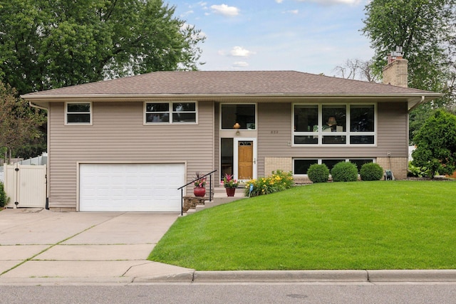 bi-level home featuring an attached garage, fence, concrete driveway, a front lawn, and a chimney